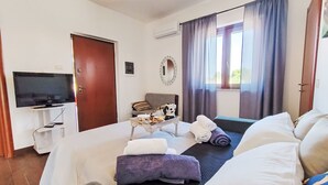 Ein Hotelzimmer mit Bett, Fernseher, kleinem Tisch mit Wasserkocher, Sofa und einem Fenster mit Vorhängen.