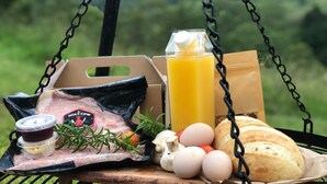 A picnic setup with a meat package, eggs, bread, a juice carton, and a bottle of sauce on a wooden table outdoors. - Nature Domes  (Toms Creek)