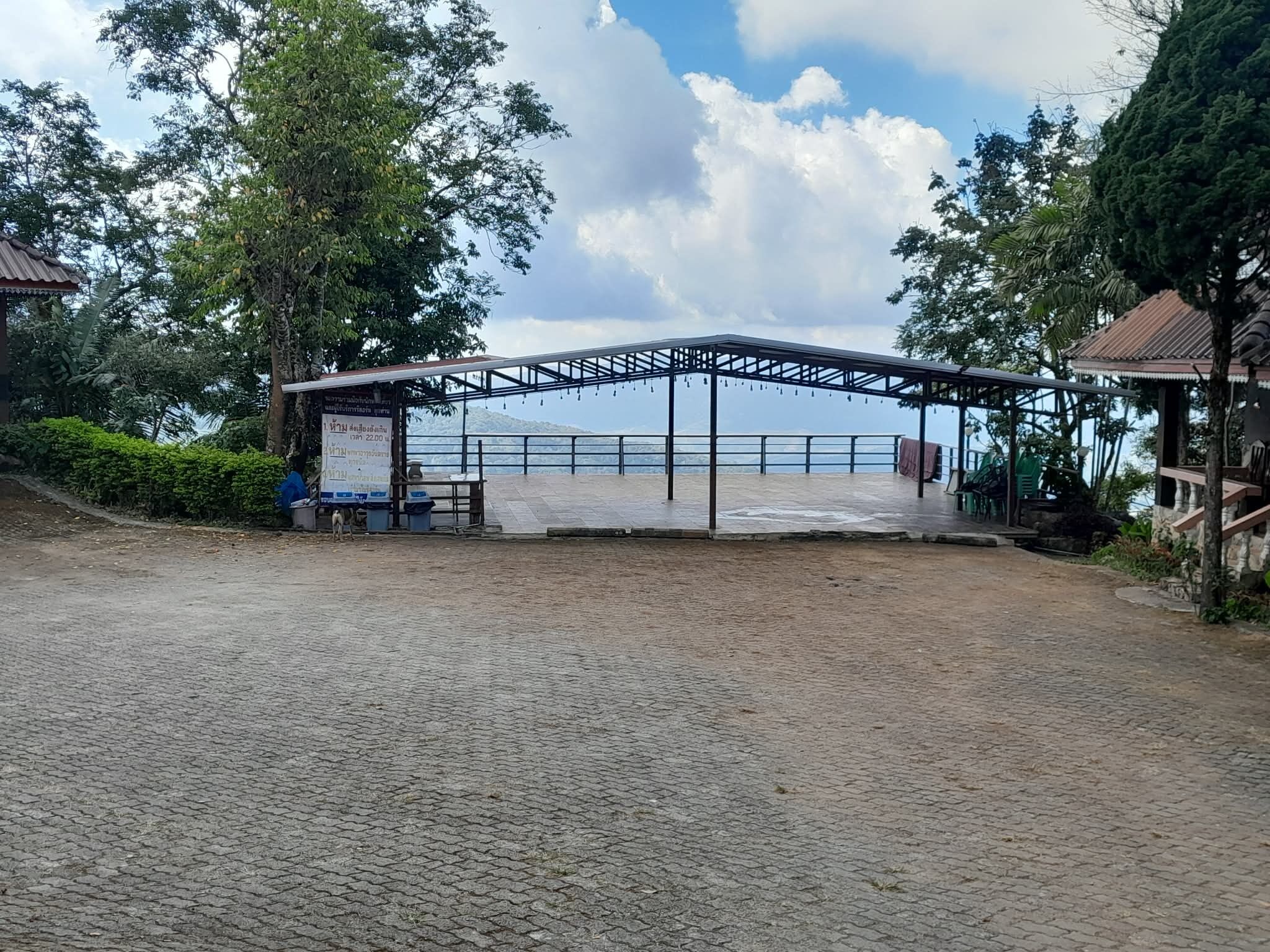 A covered outdoor area with a paved floor, a metal roof structure, and a view of the sea.