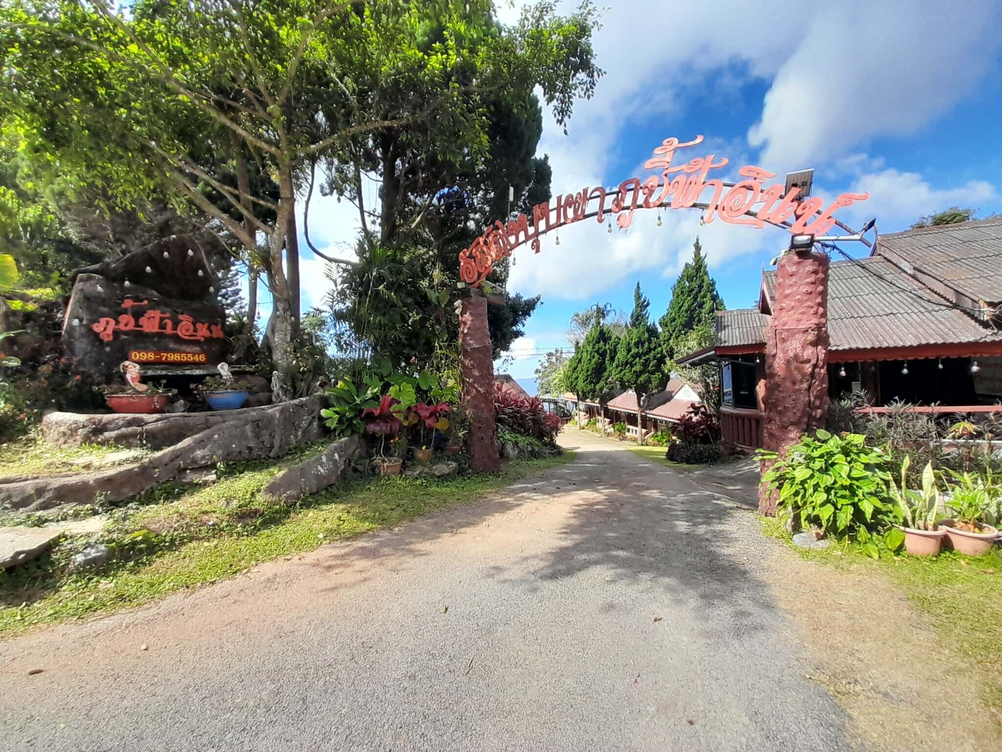 A pathway leading to a building with a traditional roof and a signboard with text.