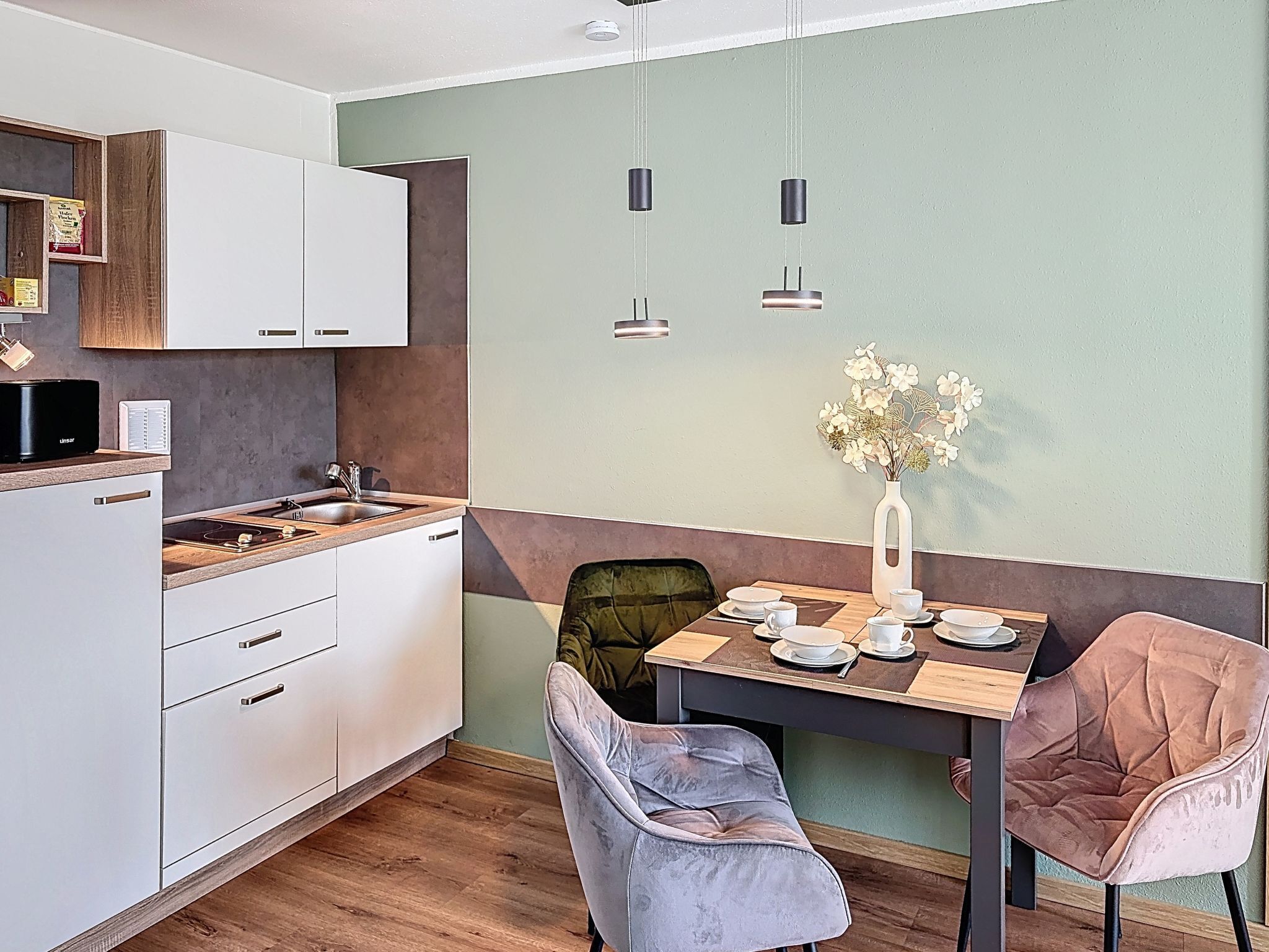 Una cocina moderna con armarios blancos, encimera de madera y un comedor con mesa para dos.