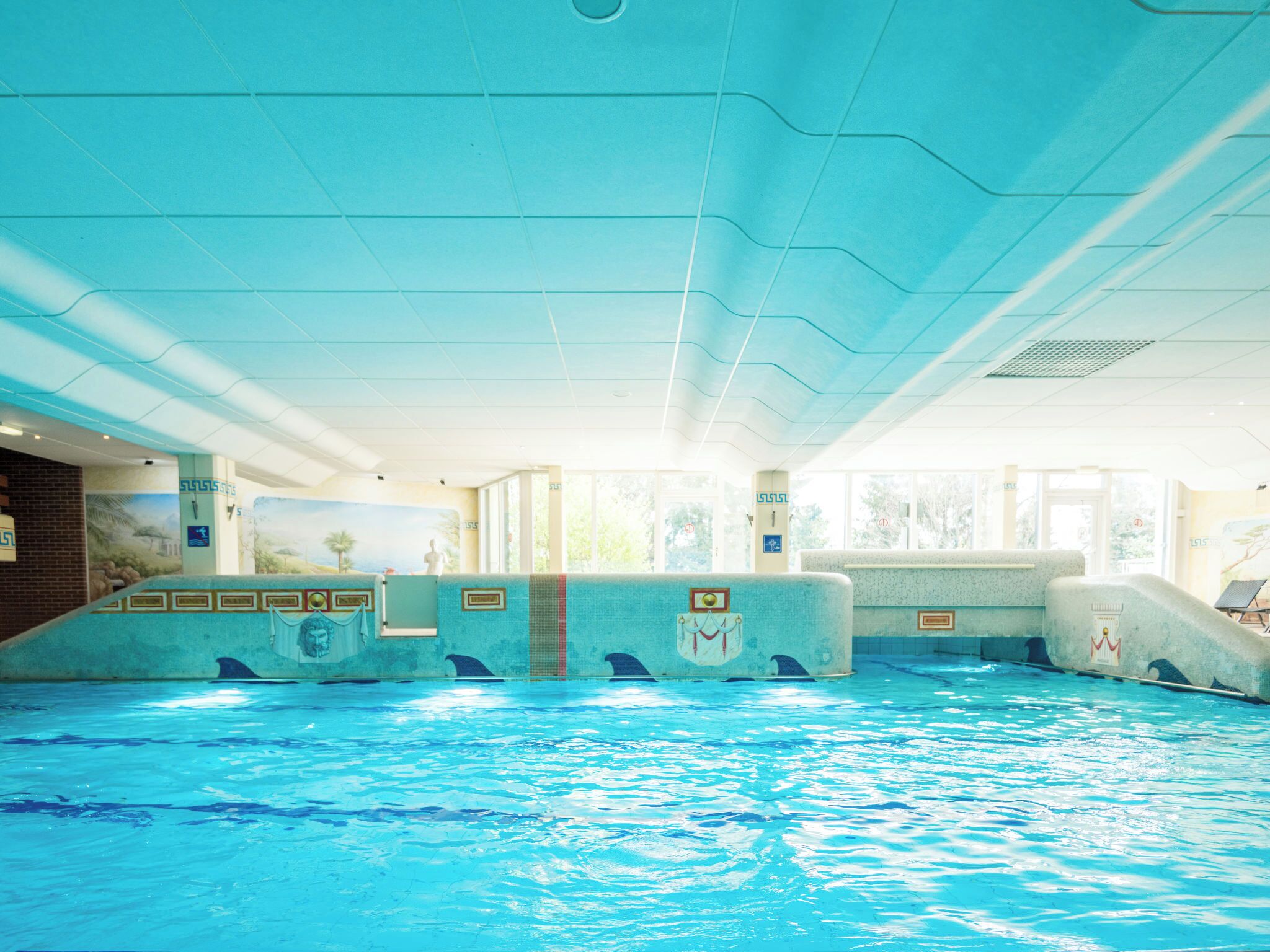 Une piscine intérieure à l’eau claire, avec des murs carrelés et des peintures murales représentant des dauphins.