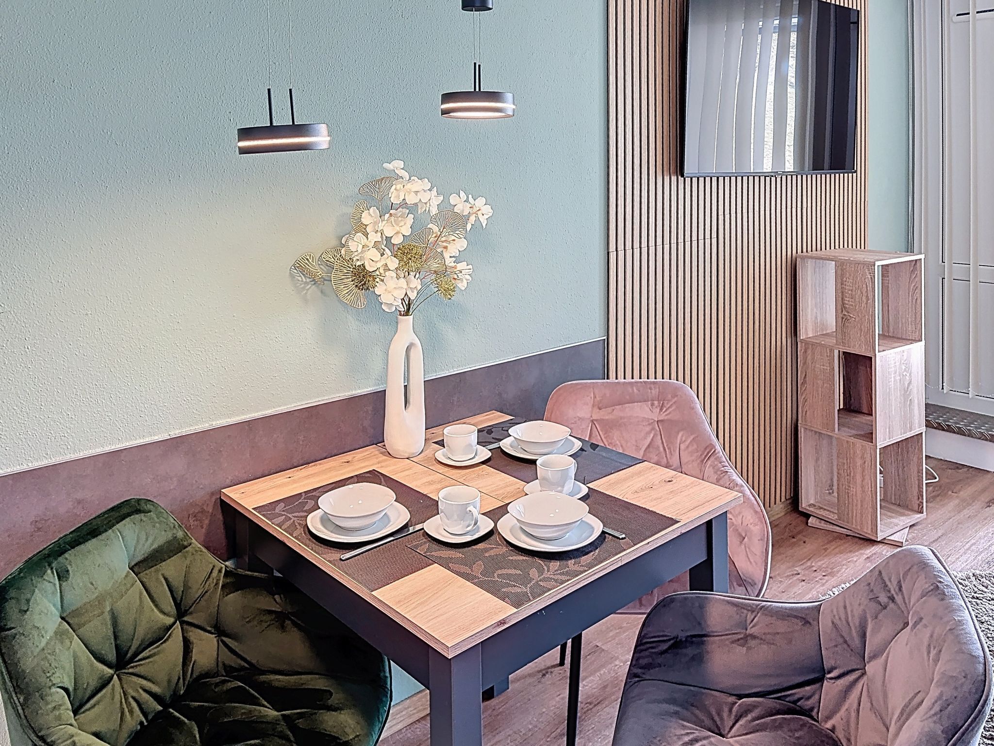 Ein Essbereich mit einem Tisch für vier Personen, einer Blumenvase und einer modernen Leuchte.