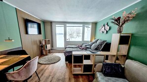 A modern, well-lit room with a wooden floor, a bed with a dark headboard, a sofa, a small table, and a TV mounted on the wall. - Nicole inkl. Schwimmbad und Sauna by Interhome (Sankt Englmar)