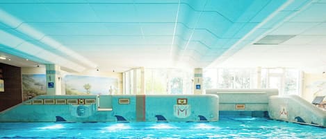 An indoor swimming pool with clear water, tiled walls, and a ceiling with a wavy design.