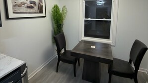 A dining area with a dark wooden table, two black chairs, a potted plant, a framed picture on the wall, and a window with blinds. - Modern Fully Renovated 2BR Retreat • Minutes from RIT • Safe & Spacious (Rochester)