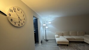 A living room with a large wall clock, a floor lamp, and a sofa. - Modern Fully Renovated 2BR Retreat • Minutes from RIT • Safe & Spacious (Rochester)