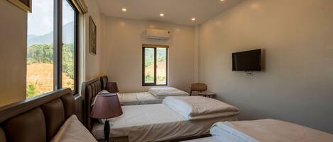 A hotel room with three beds, a television, and a window with a view of greenery.