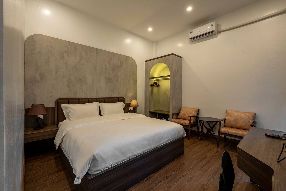 A bedroom with a large bed, a desk, a chair, and a small table.
