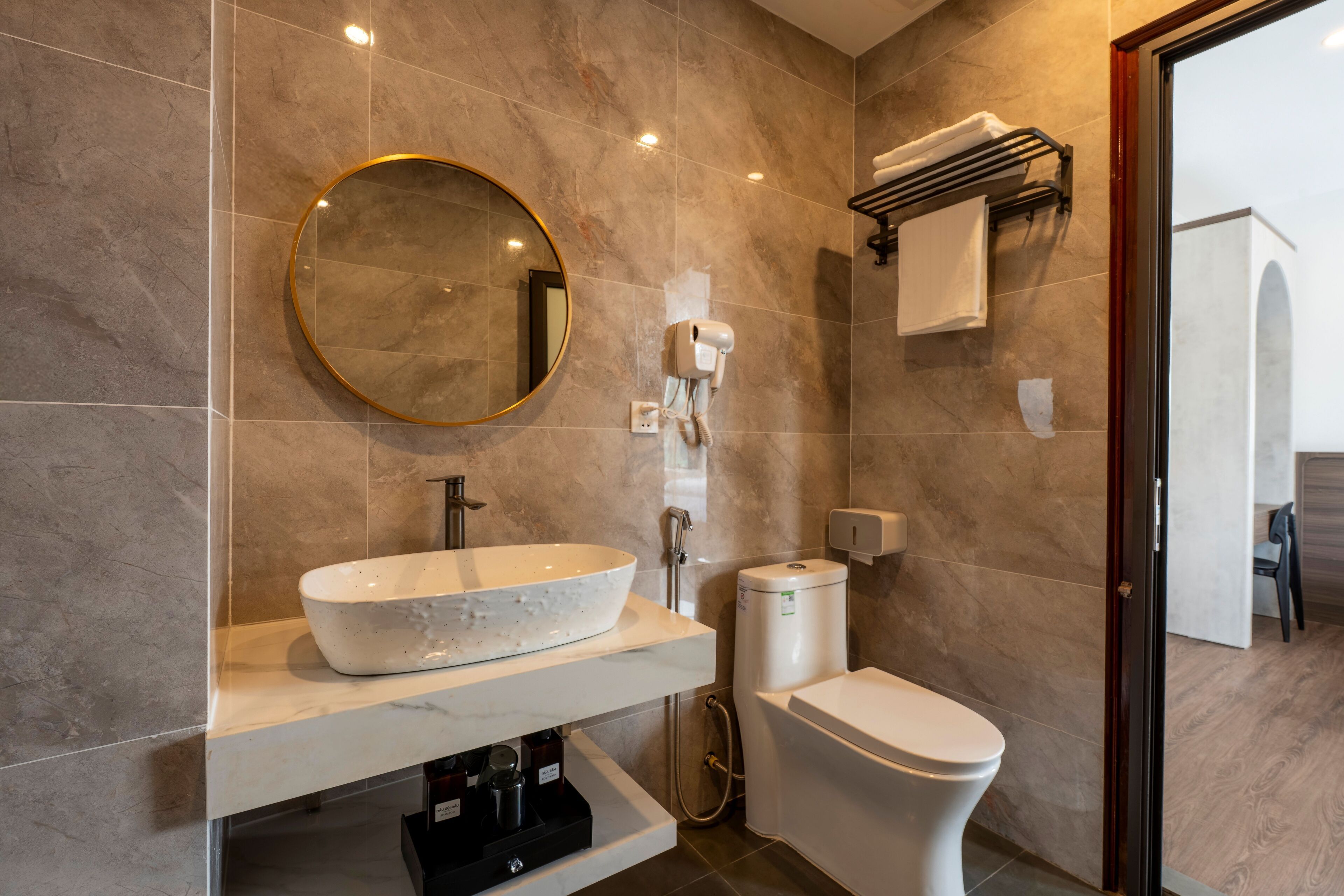 Une salle de bain moderne avec un grand miroir ovale, un lavabo sur colonne, des toilettes et un porte-serviettes.