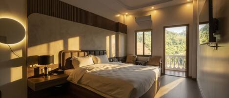 A modern hotel room with a large bed, bedside lamps, a nightstand, a chair, and a balcony with a view of greenery.
