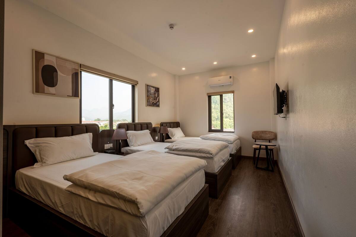 A hotel room with three beds, a TV, and a window with a view.