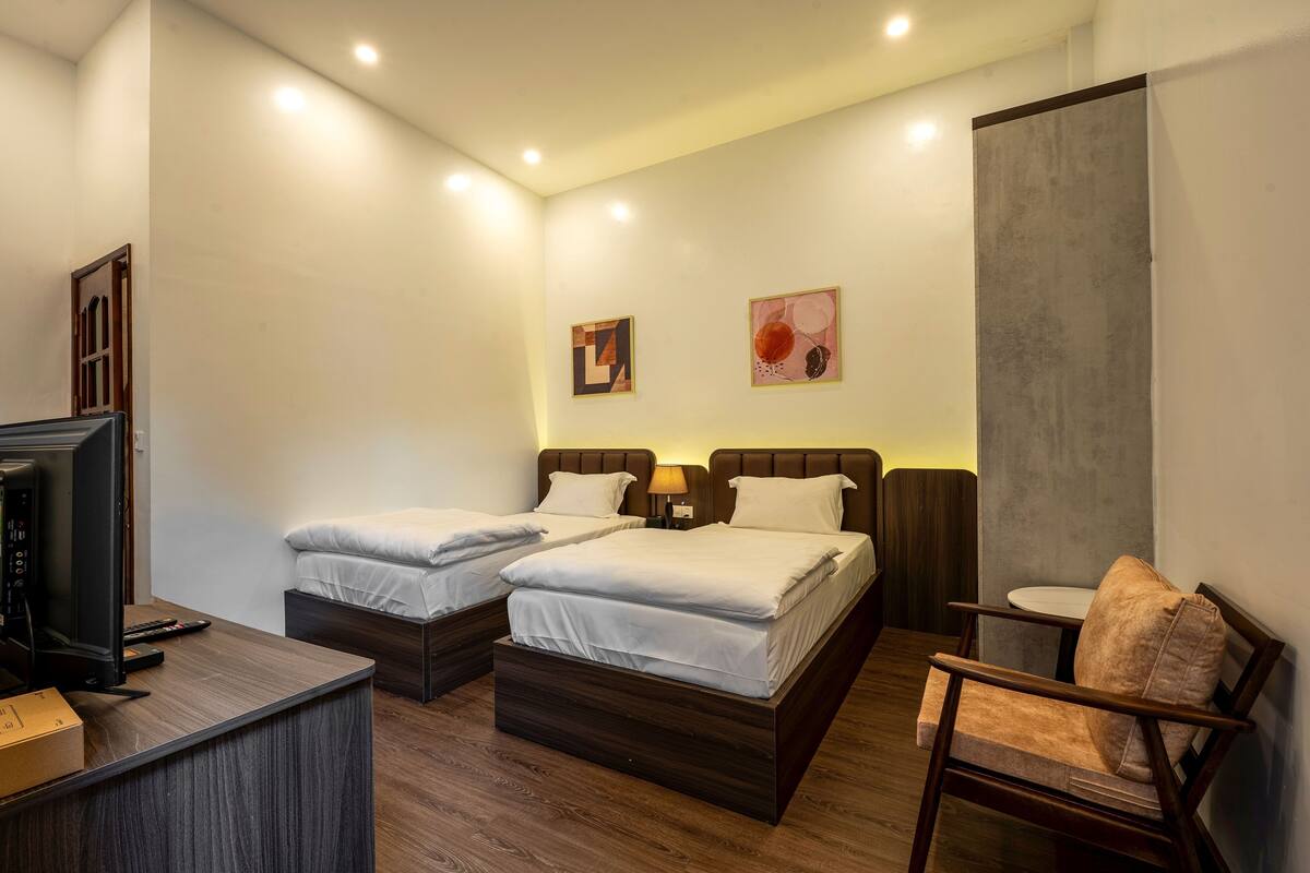 A hotel room with two beds, a desk with a computer, a chair, and artwork on the walls.