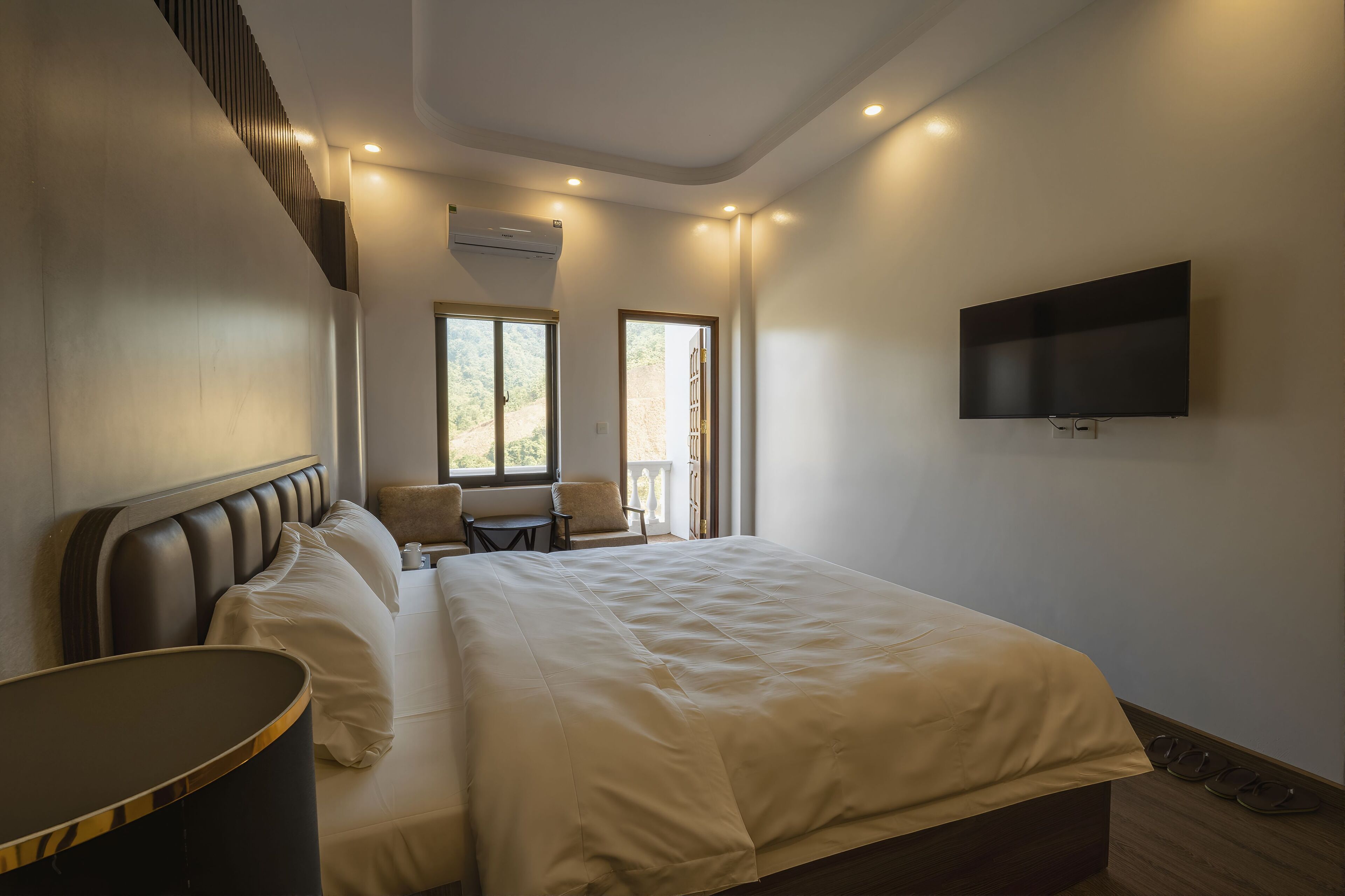 A modern hotel room with a large bed, a flat-screen TV, and a seating area with a chair and table.