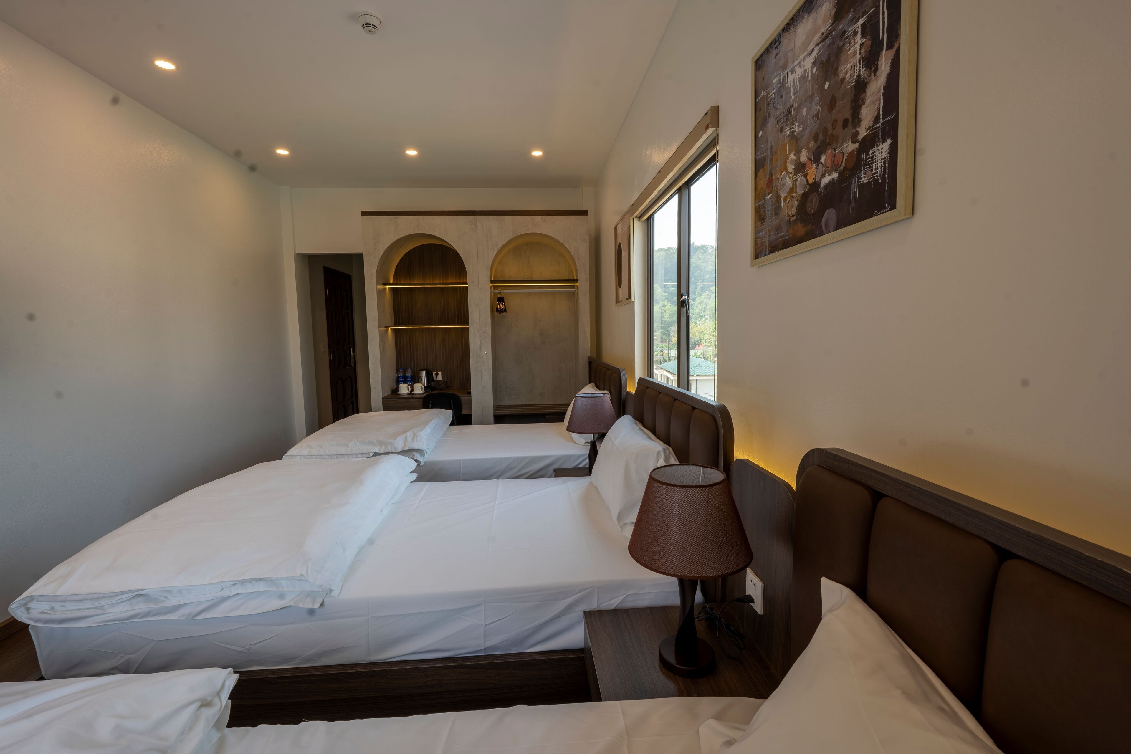 A hotel room with two beds, a window, and a painting on the wall.