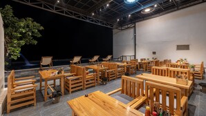 A spacious room with multiple wooden tables and chairs, a large potted plant, and a stage area. - Odyssey Hotel 2 (Ha Giang 1)