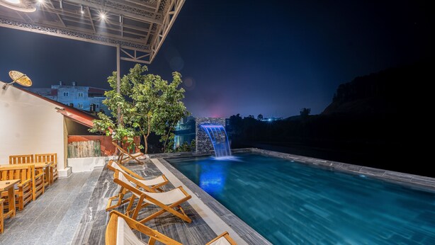 A poolside area with lounge chairs, a waterfall feature, and a view of the cityscape at night. - Odyssey Hotel 2 (Ha Giang 1)