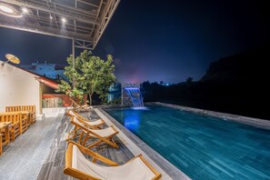 A poolside area with lounge chairs, a waterfall feature, and a view of the cityscape at night. - Odyssey Hotel 2 (Ha Giang 1)