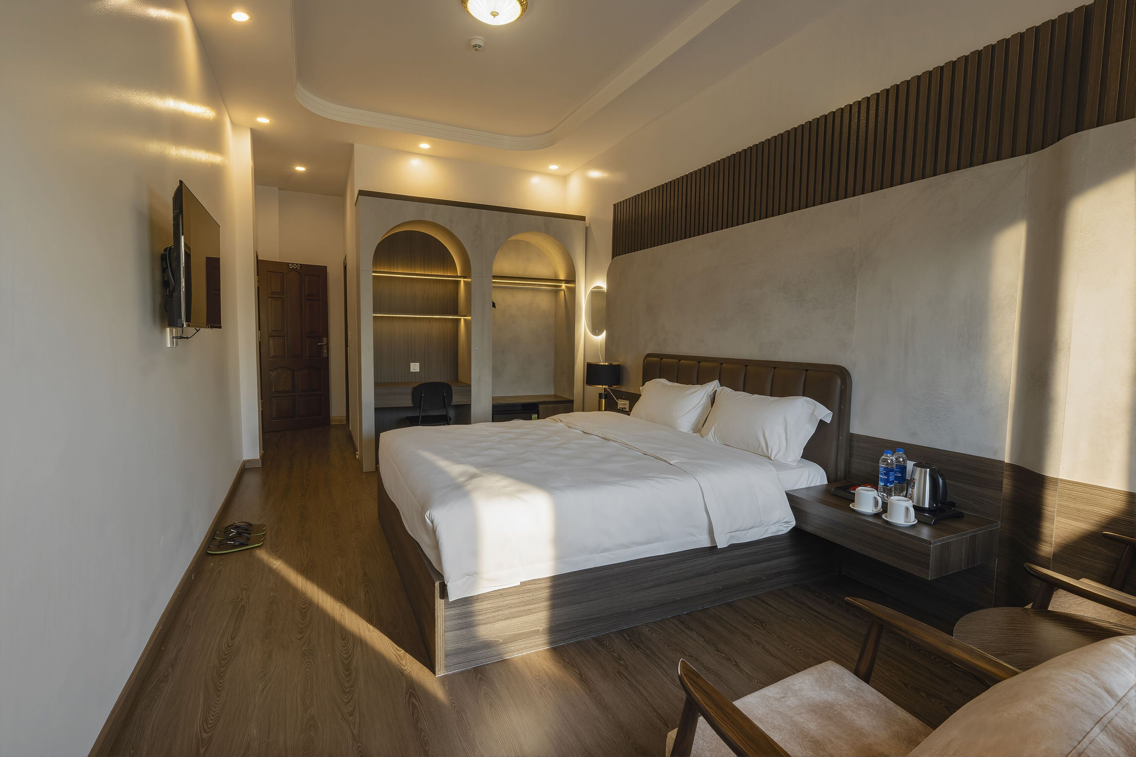 Habitación de hotel moderna con una cama grande, una mesita de noche con artículos de tocador, un armario y un televisor montado en la pared.