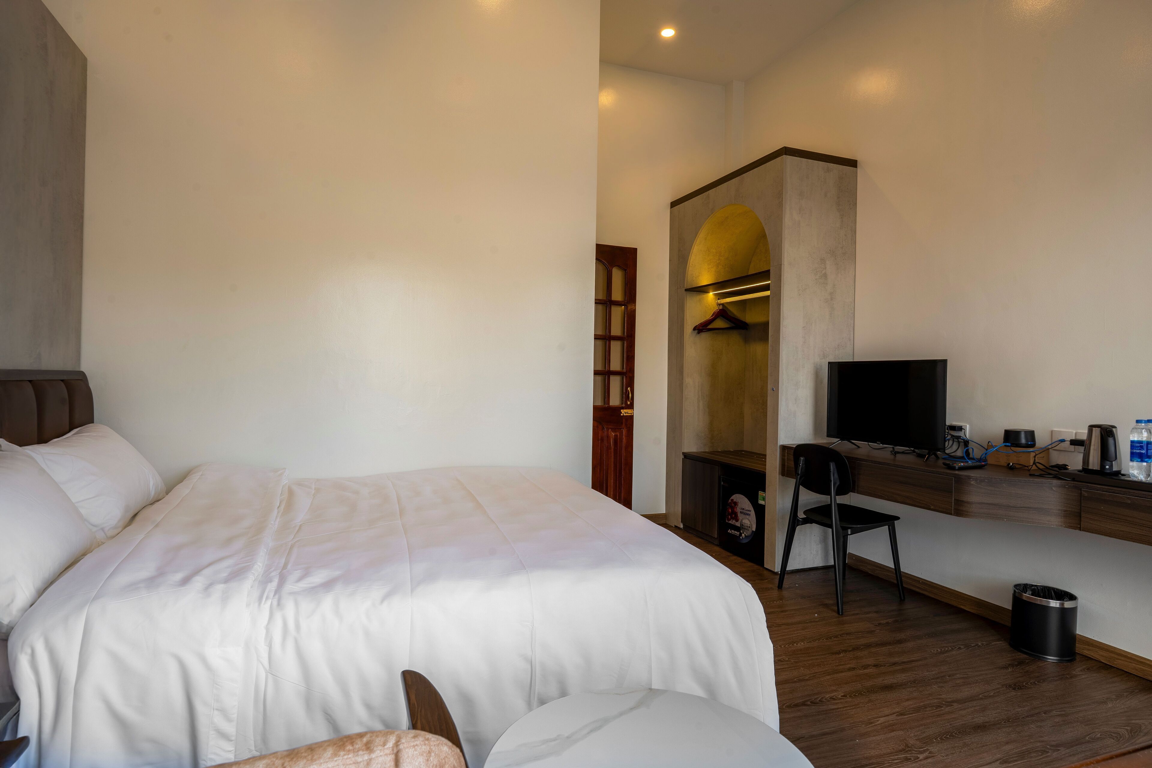 Una habitación de hotel con una cama grande, un escritorio con televisión, una silla y un bote de basura pequeño.