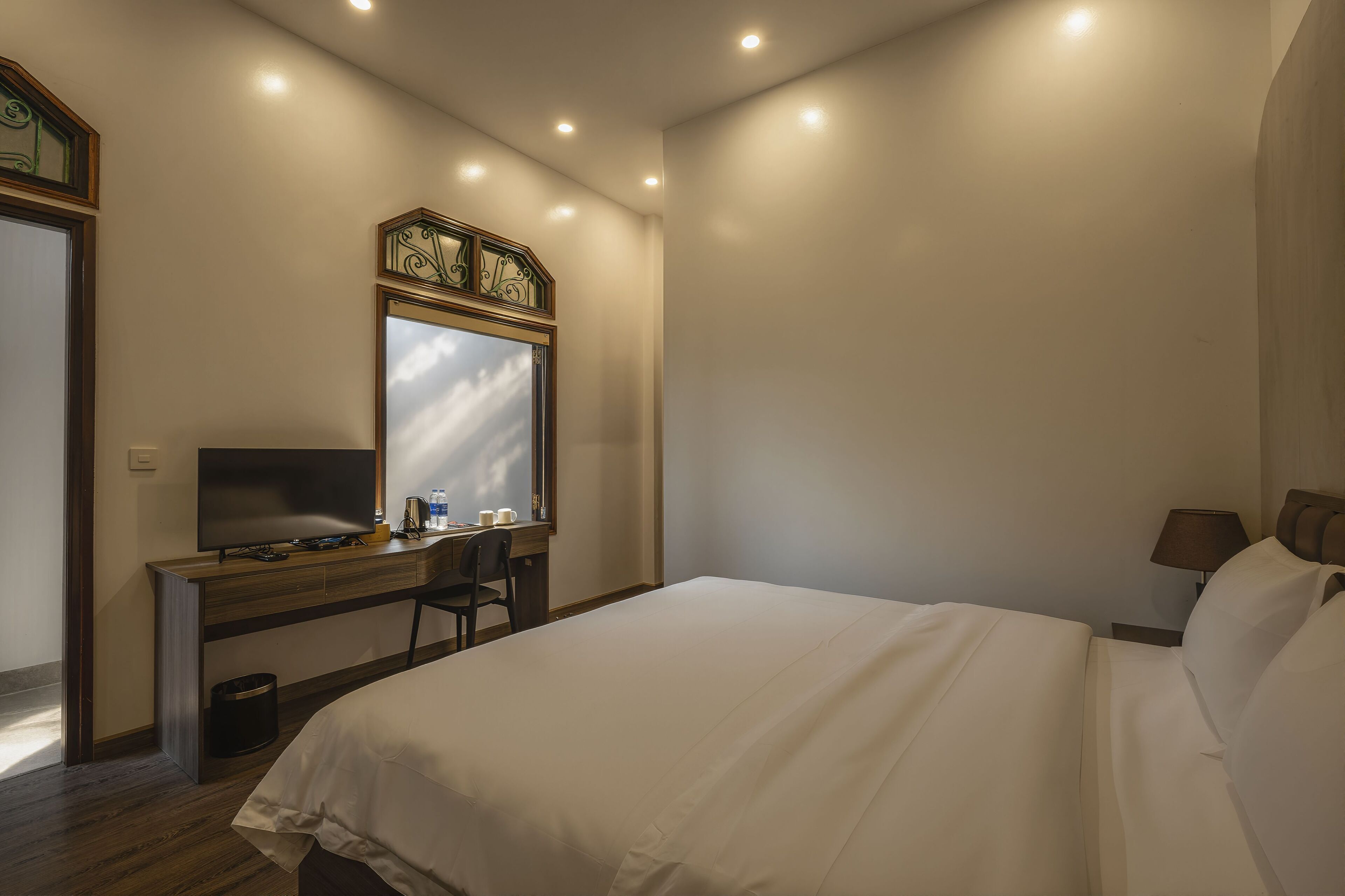A hotel room with a bed, a desk with a computer, a chair, and a window.