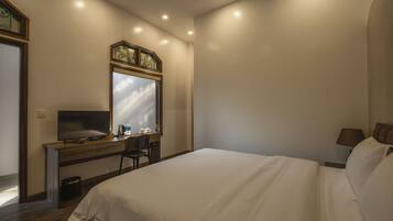 A hotel room with a bed, a desk with a computer, a chair, and a window.