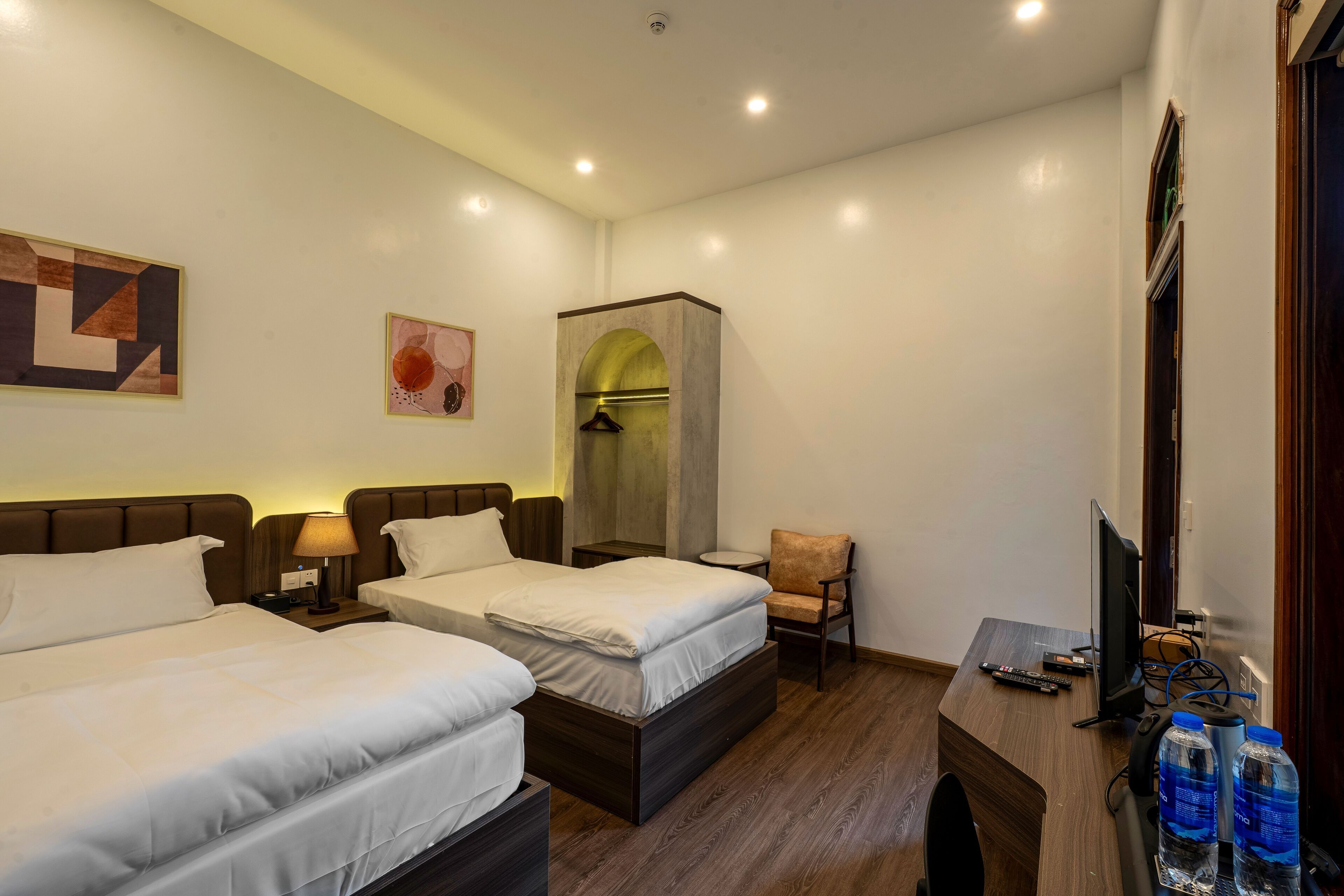 Een hotelkamer met twee bedden, een bureau, een stoel, een televisie en een kledingkast.