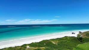 A beach with clear turquoise waters, a sandy shore, and a vehicle parked on the beach.
