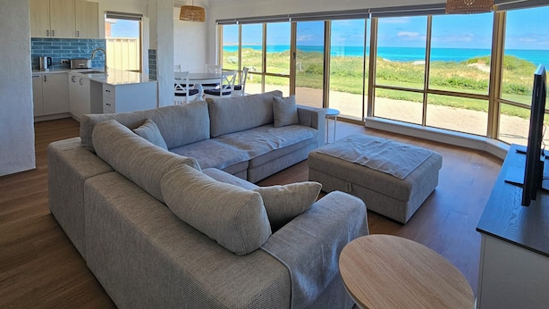 A modern living room with a large sectional sofa, a small round table, and a view of the ocean.