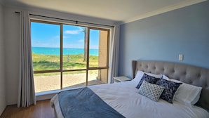A bedroom with a large bed, a view of the beach, and a brick wall.