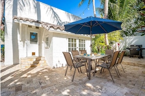 Une terrasse avec une table et des chaises, un parasol bleu et un barbecue.