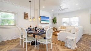 A dining area with a round table, white chairs, pendant lighting, and a view of the outdoors. - Beach House on the Beach for 8 People With Jacuzzi (Hollywood)