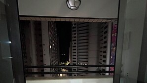 A balcony with a round table and two chairs, a small rug, and a view of buildings at night. - Beira Mar Apartment - Fortaleza (Fortaleza)