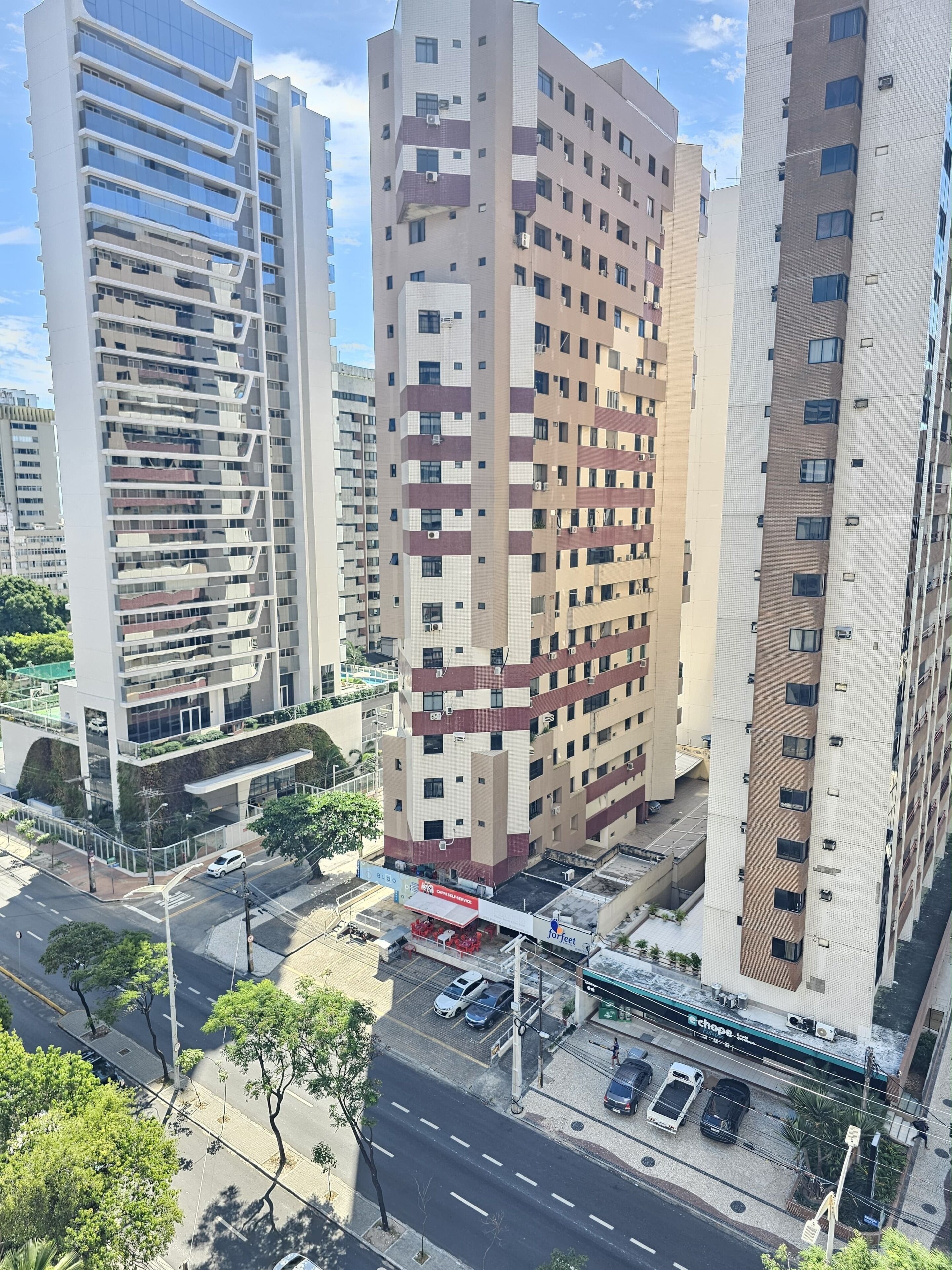 Um edifício alto com vários andares, uma área de estacionamento e uma rua com carros.