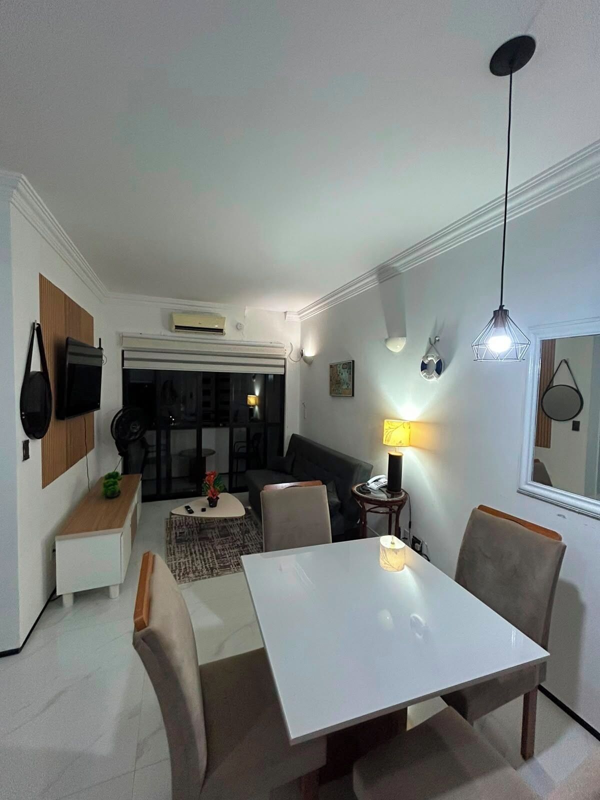 A modern living room with a dining area, featuring a white table, comfortable seating, and a large window.