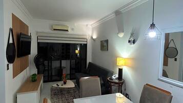 A modern living room with a dining area, featuring a white table, comfortable seating, and a large window.