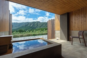 Un área de spa moderna con techo de madera, tinaja de piedra y vistas a un paisaje montañoso.