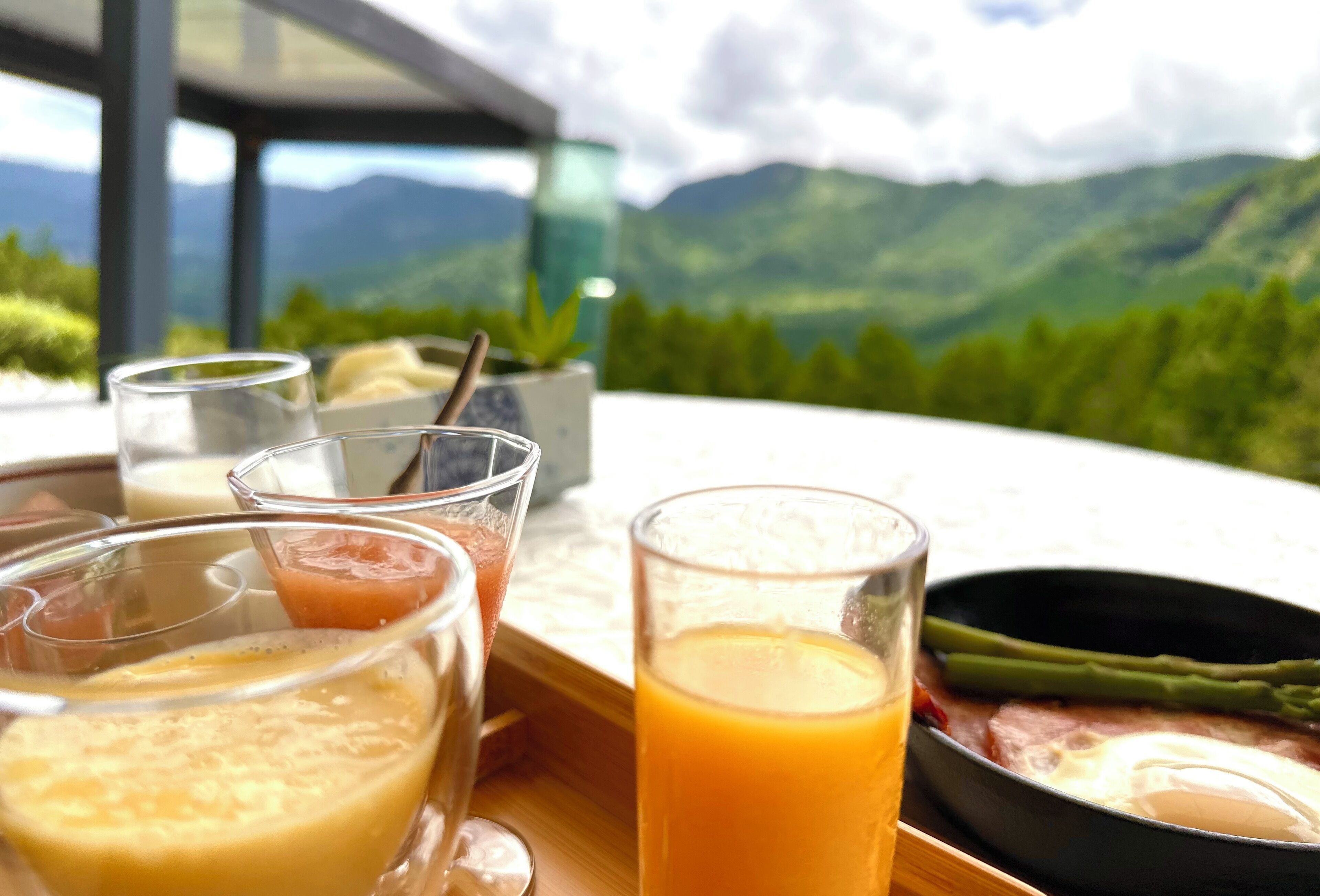 Bandeja de desayuno con diversas bebidas y una fuente de comida, frente a una vista panorámica de las montañas.