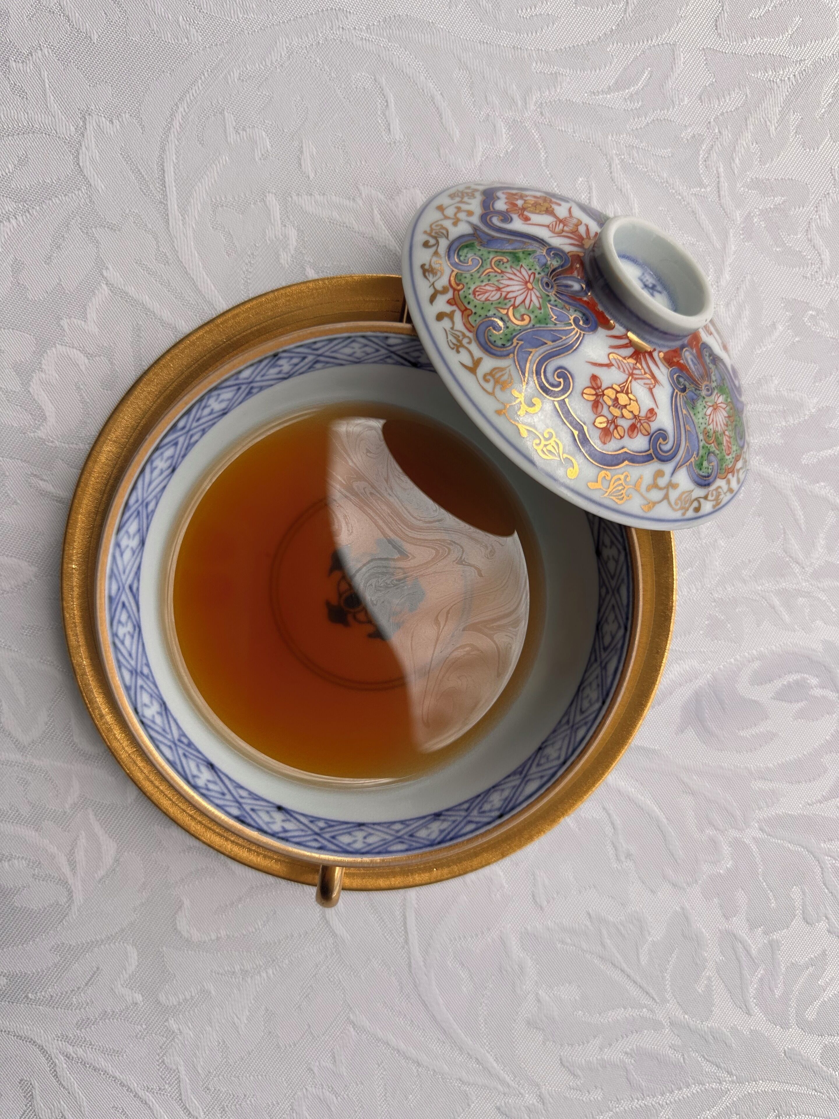Une théière avec un couvercle, posée sur une table recouverte d’une nappe à motifs.