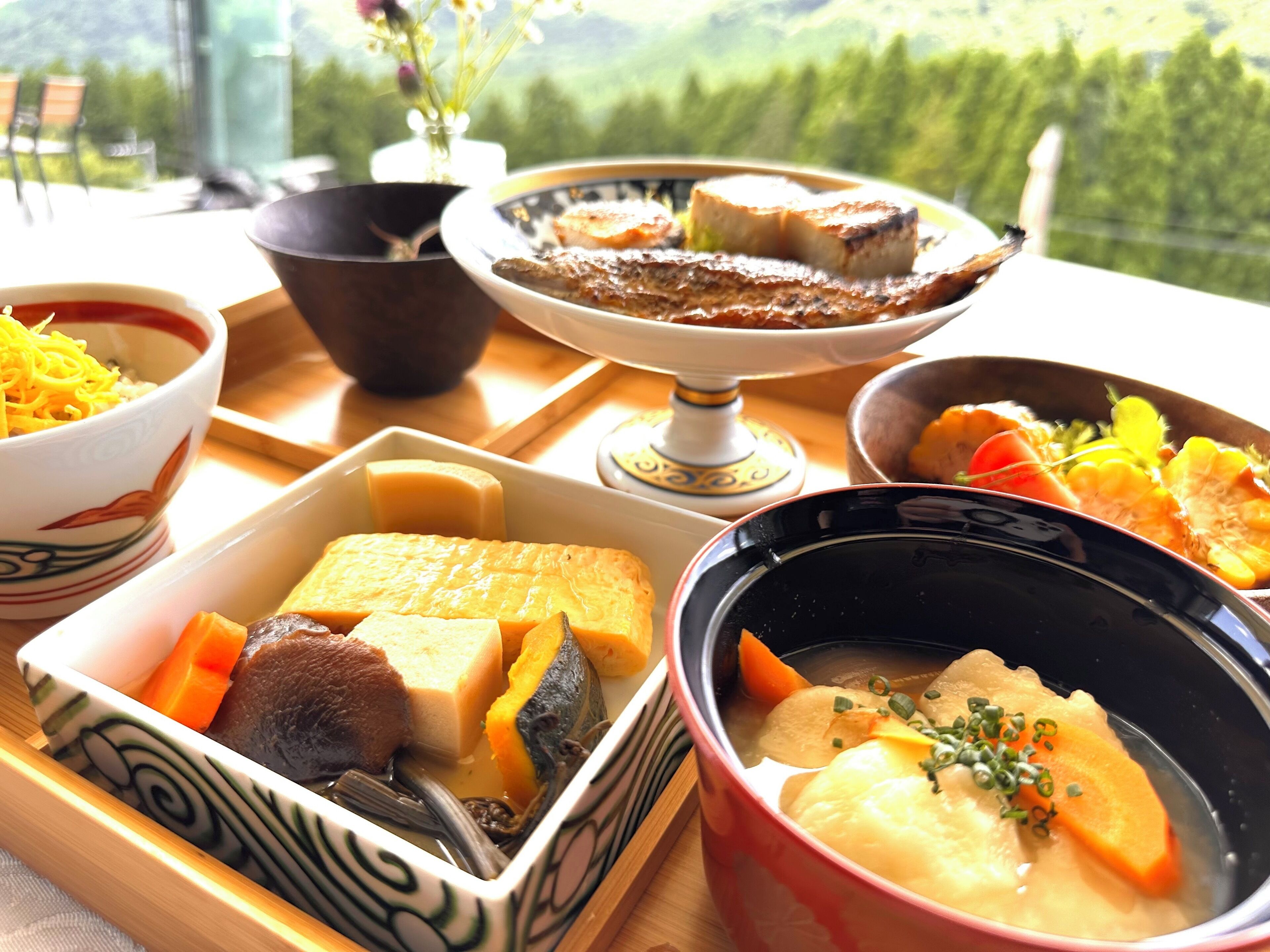 A variety of dishes on a table, including a bowl of soup, a dish with tofu and vegetables, and a plate with grilled fish.