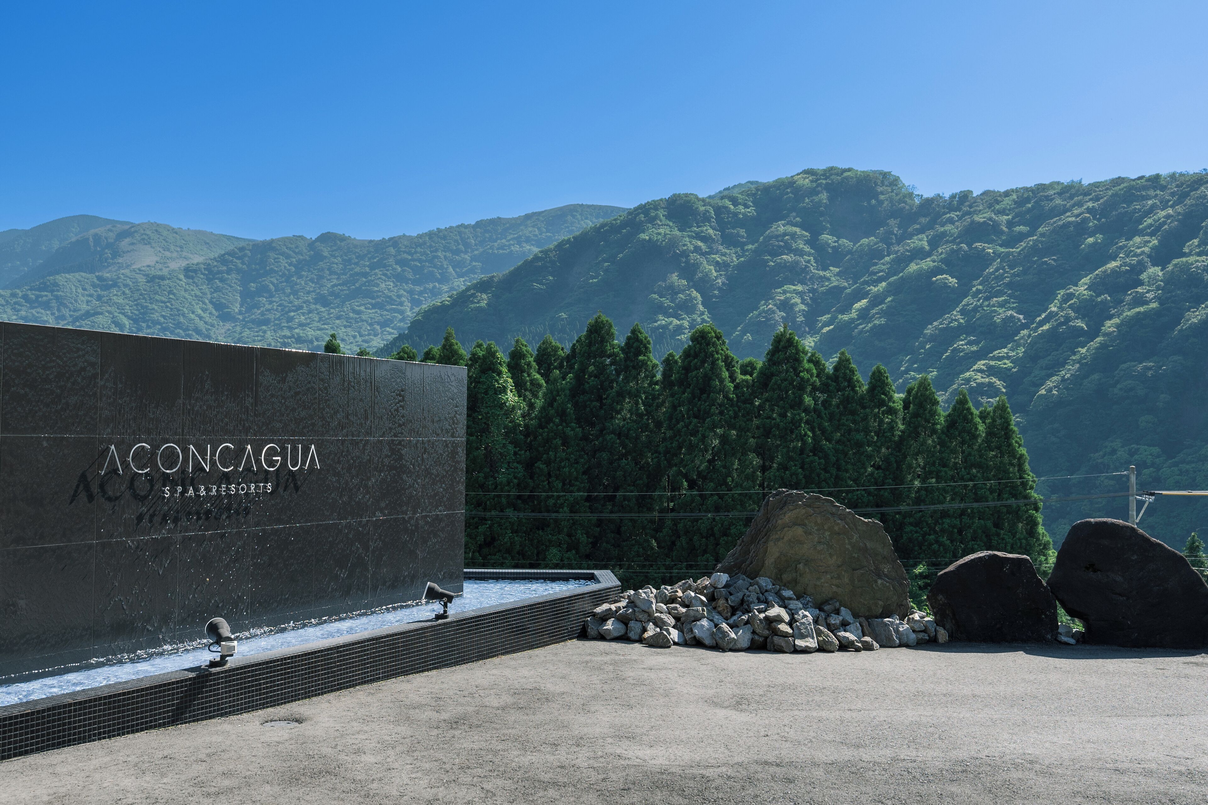 A spa area with a large stone wall, a pool, and a view of a forested mountain range.