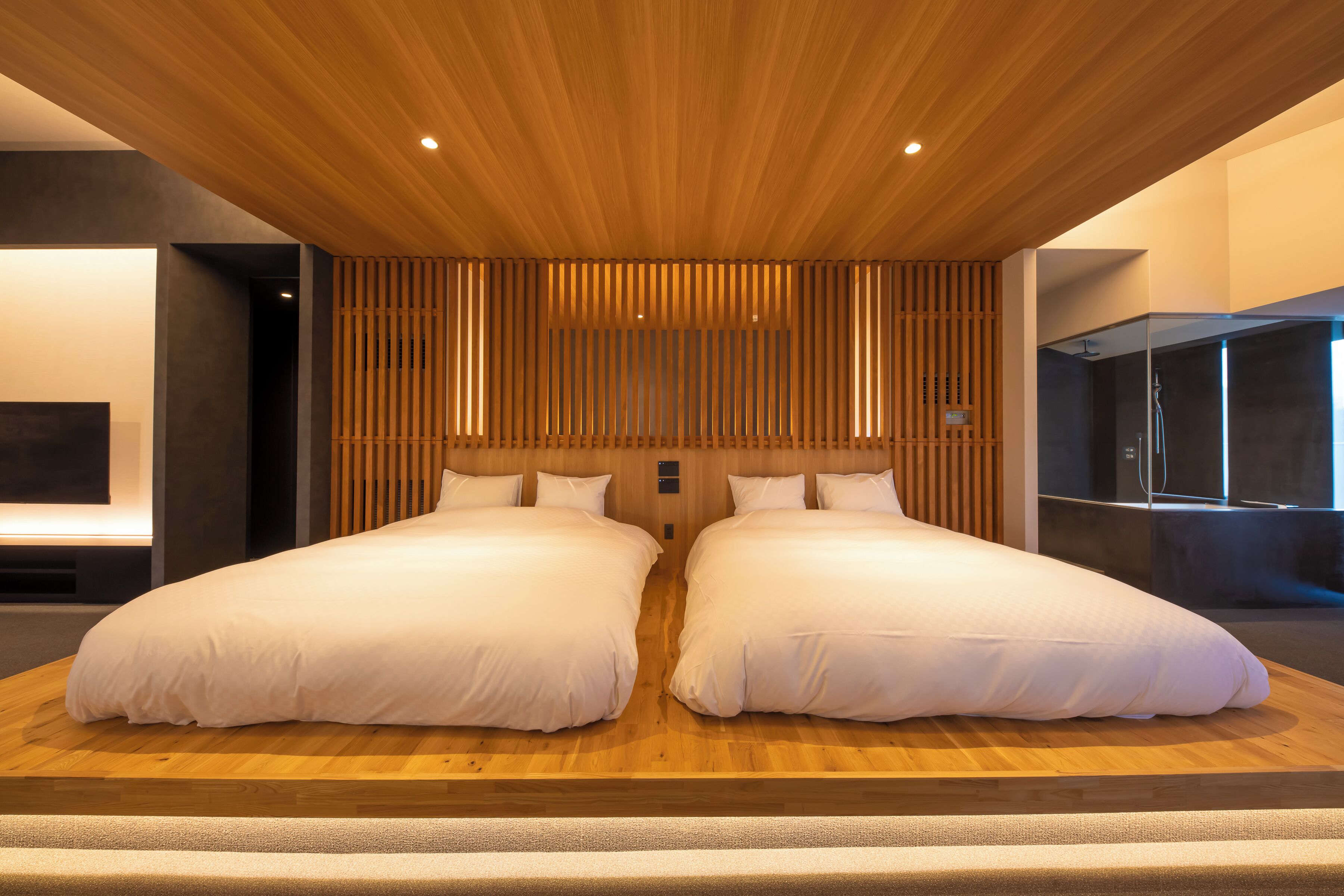 A modern hotel room with a large bed, wooden ceiling, and a TV mounted on the wall.