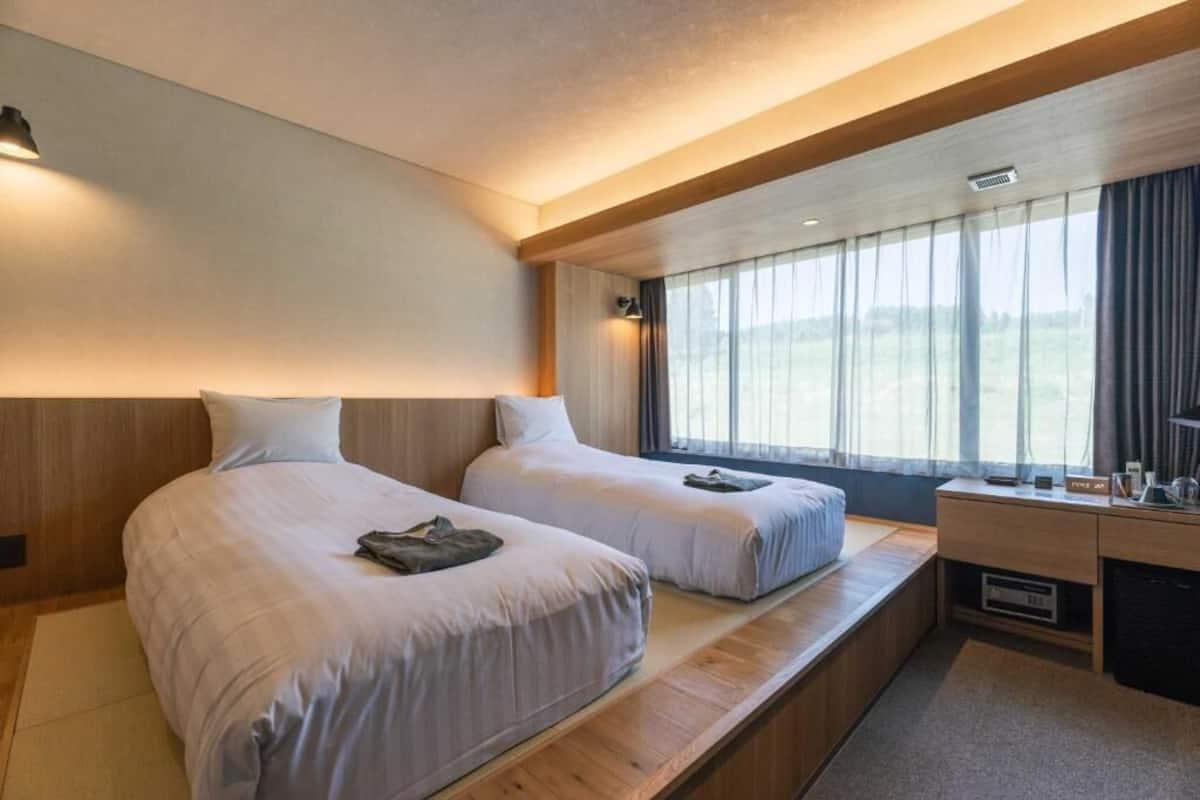 Une chambre d’hôtel moderne avec deux lits, un bureau et une grande fenêtre avec des rideaux.