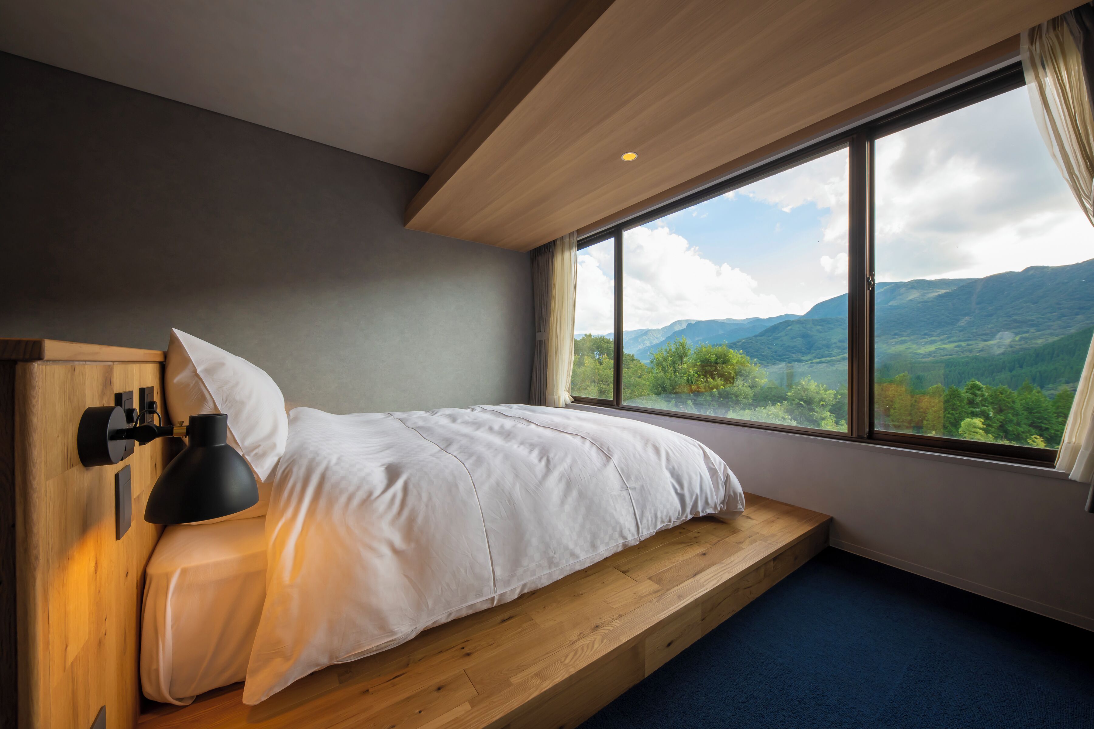A bedroom with a bed, a nightstand, a lamp, and a large window offering a mountain view.