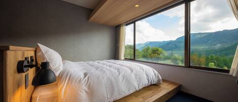 A bedroom with a bed, a nightstand, a lamp, and a large window offering a mountain view.