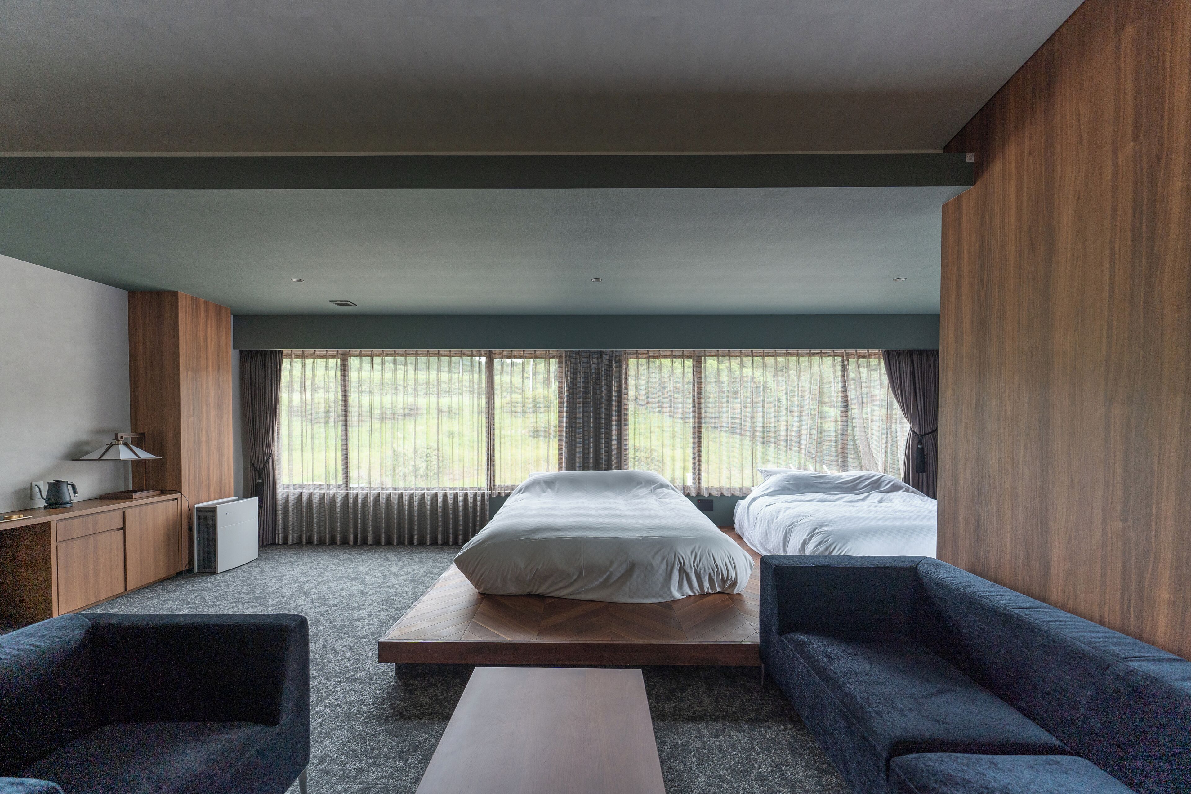 Et moderne hotelværelse med seng, to sofaer, et sofabord og et skrivebord med lampe.