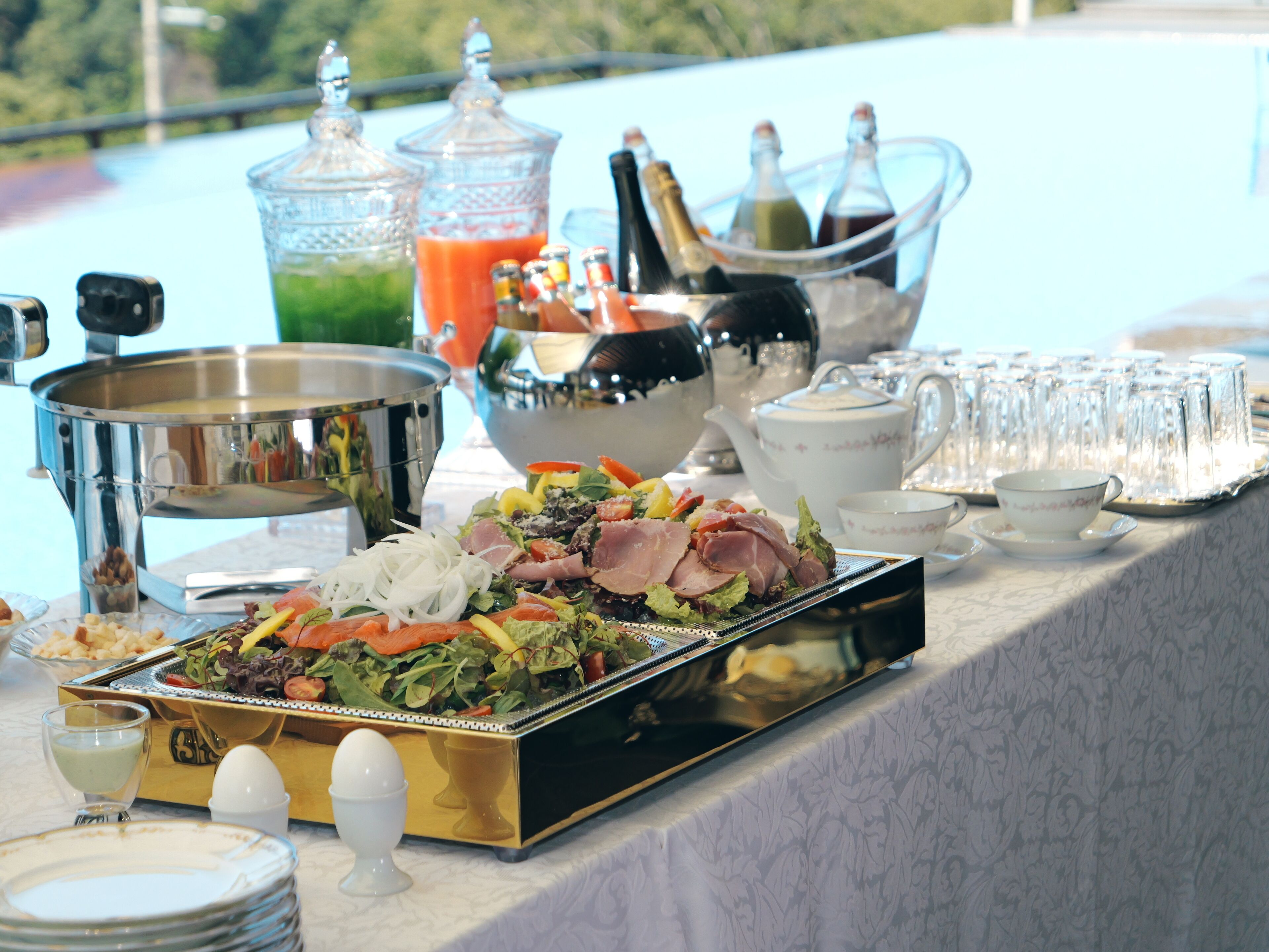 A buffet table with various food items and beverages, including a salad, meats, and a selection of drinks in a glass container.