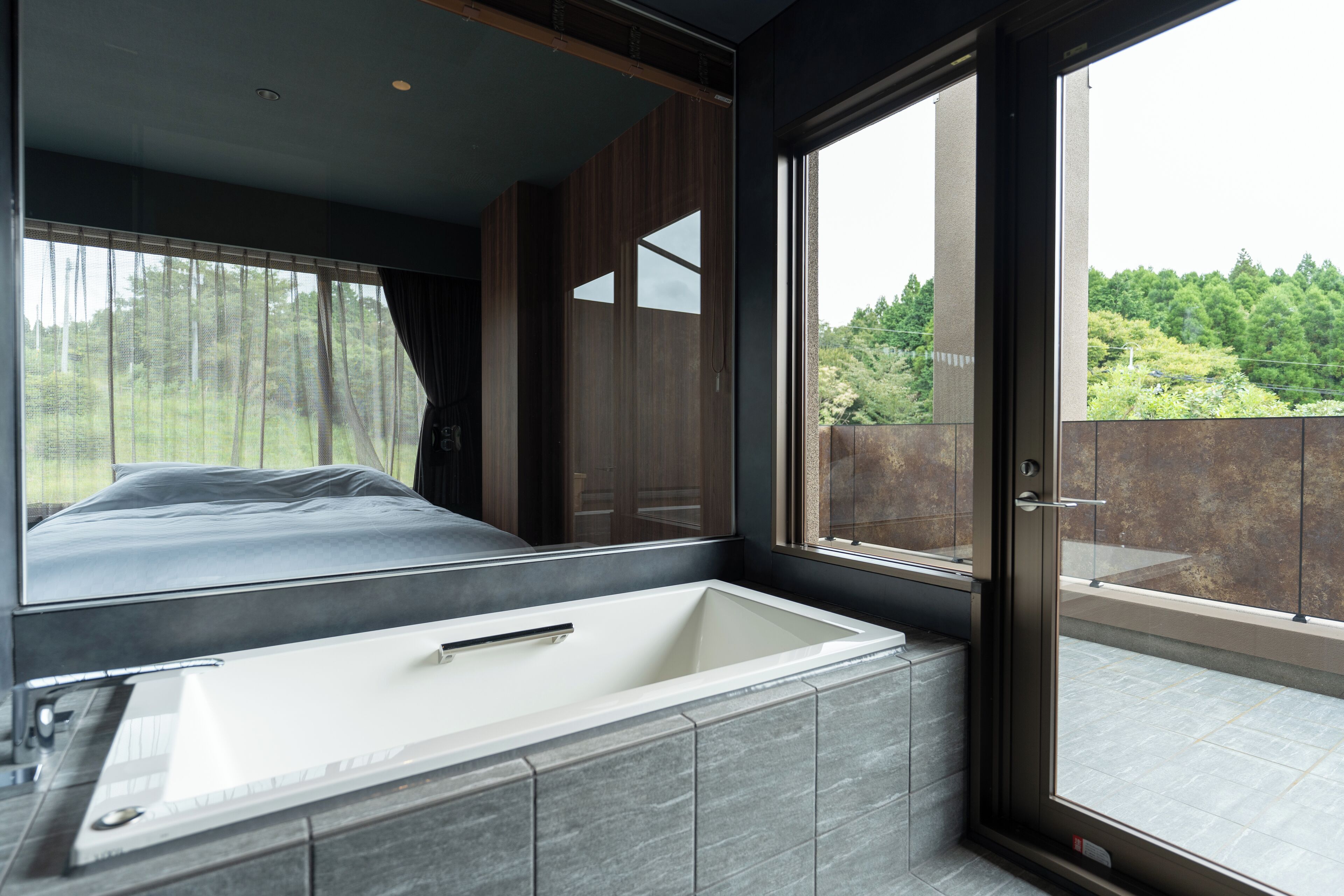A modern bathroom with a large bathtub, a mirror, and a view of greenery outside.