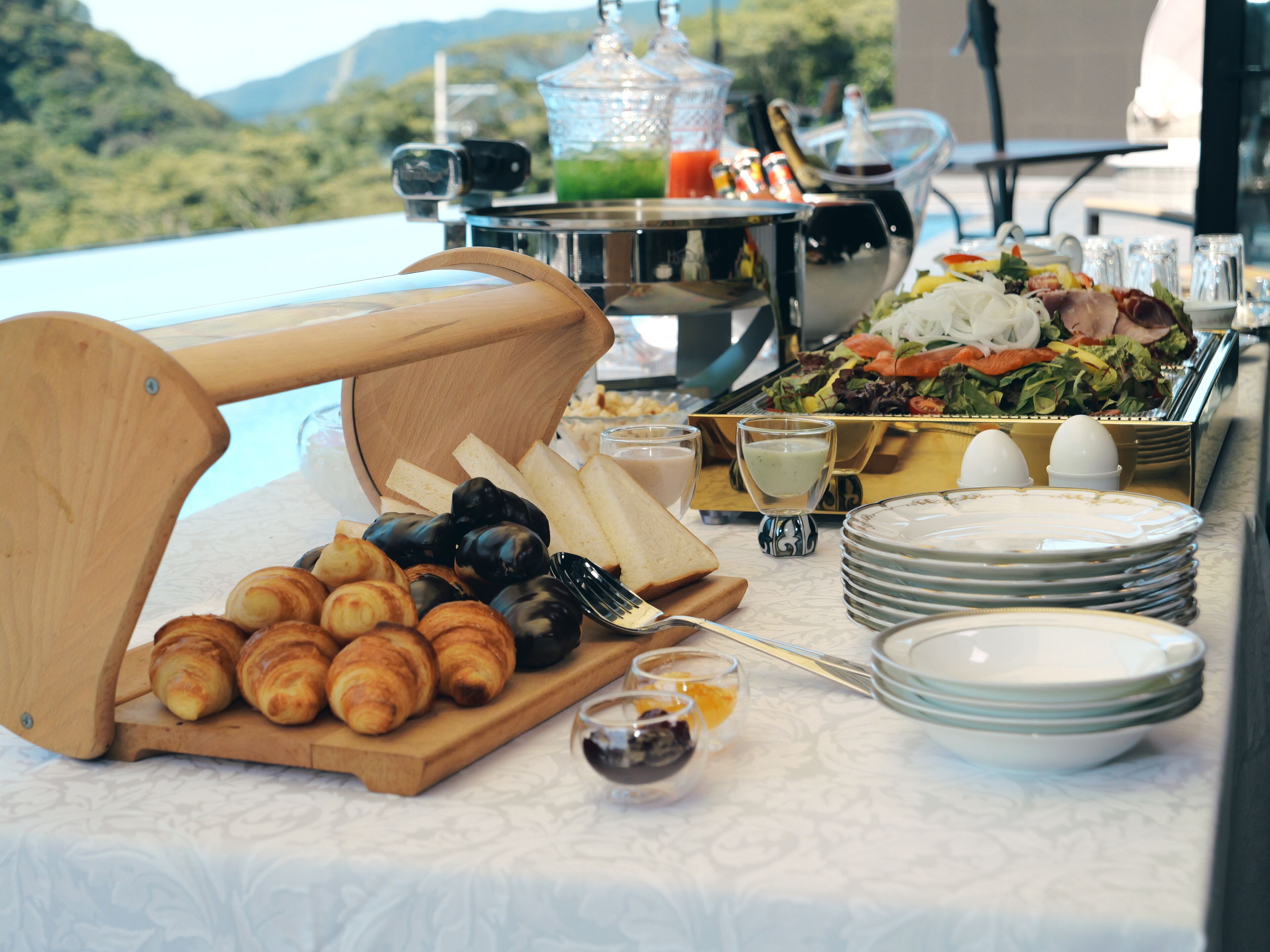 A buffet table with croissants, bread, and a salad.