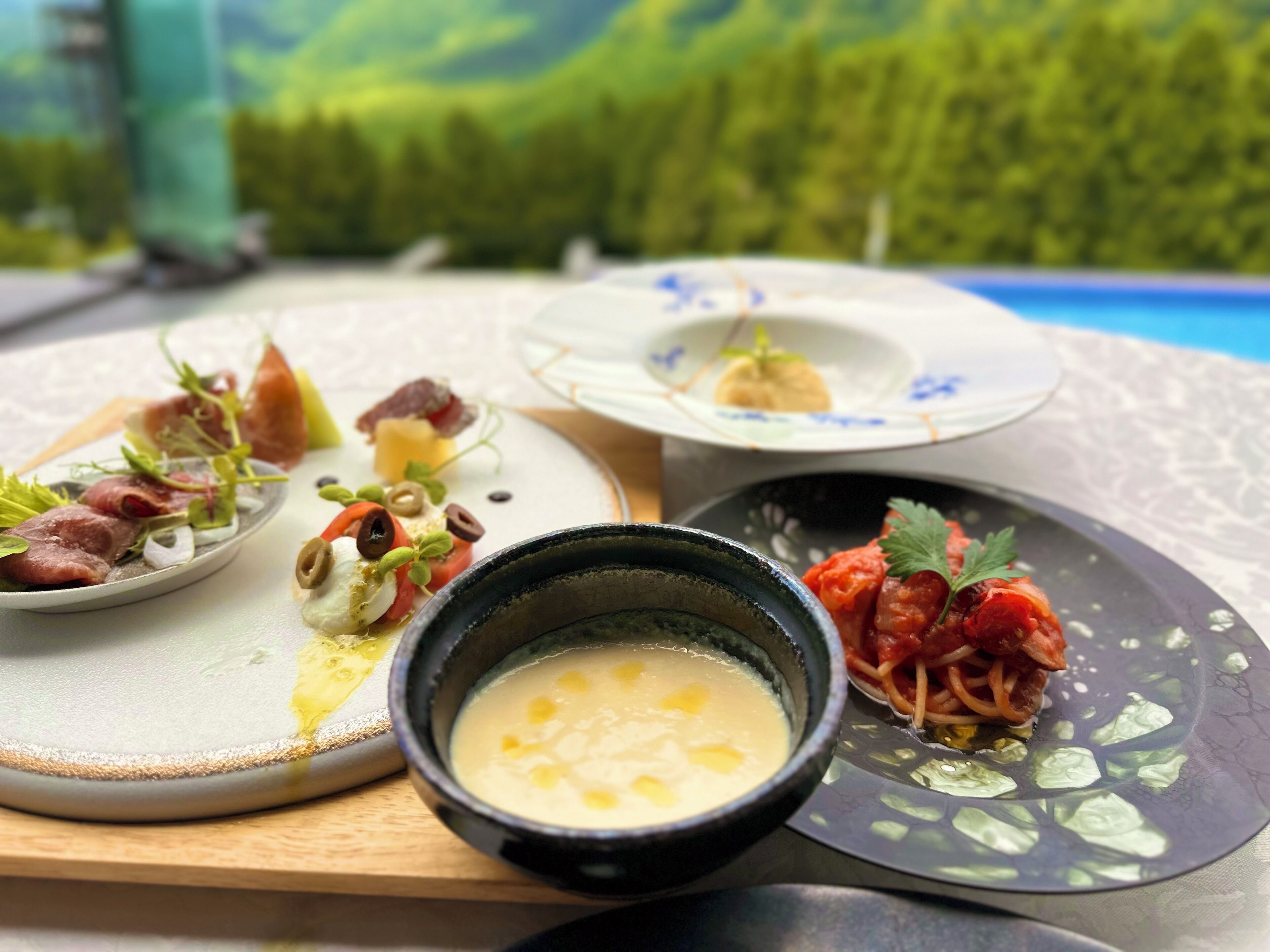 Ein Tisch mit verschiedenen Speisen, darunter eine Suppenschüssel, ein Teller mit Gemüse und Fleisch sowie ein Teller mit Dessert.